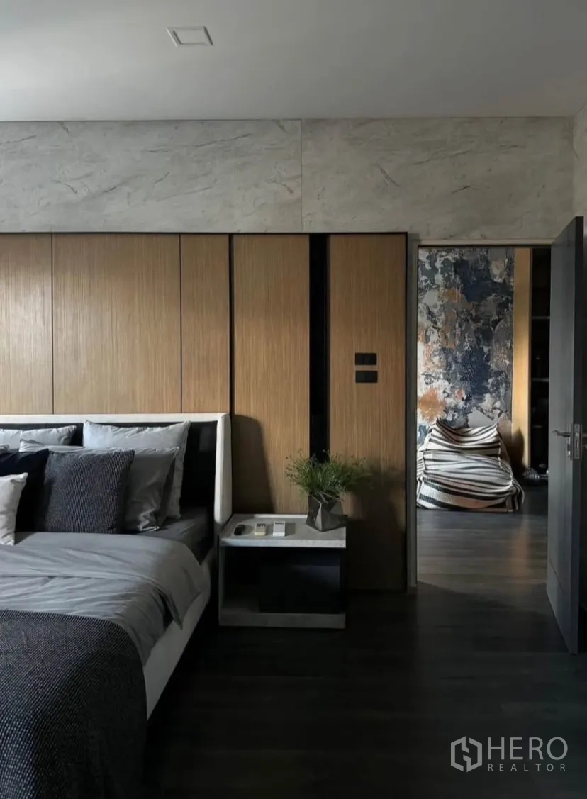 Townhouse for rent or sale in Bang Phli, Samut Prakan - Master bedroom with wood-paneled wall, grey bedding and bedside table leading to a cozy nook.