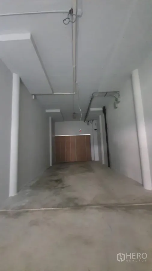 零售空间 出租在Khlong Toei, Bangkok - 长条形开放式零售空间，水泥地、高挑天花与外露管线，尽头为卷帘门。