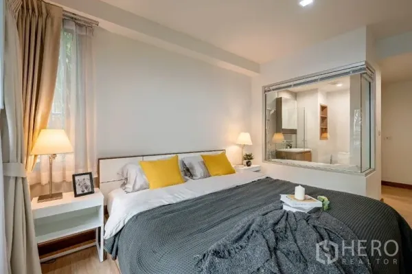 Condominium for sale - Master bedroom with king bed, bedside lamps and a glass window looking into a bathroom with tub.