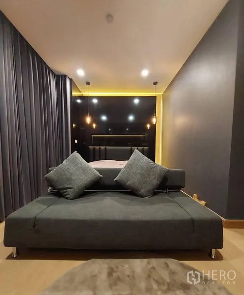 Townhouse for rent in Thanyaburi, Pathum Thani - Cozy bedroom with dark accent wall, pendant lights, and a gray sofa at the foot of the bed.