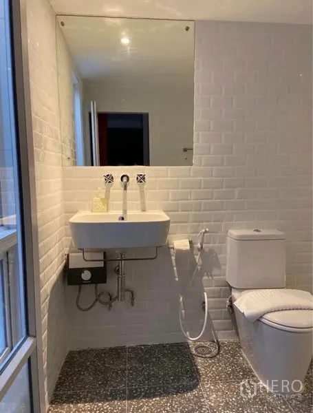 Townhouse for rent in Khlong Toei, Bangkok - Bright bathroom with white subway tiles, large mirror, wall‑mounted sink and toilet.