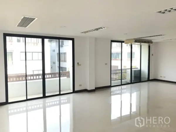 Home Office for rent in Wang Thonglang, Bangkok - Spacious workspace with floor-to-ceiling sliding doors to two balconies and a wall-mounted air conditioner.