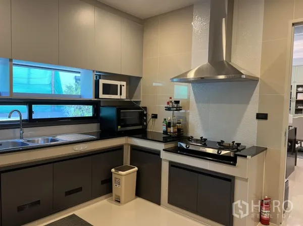 Detached House for rent or sale in Bang Kapi, Bangkok - Fully fitted Thai kitchen with L-shaped counters, double sink, gas cooktop with hood, microwave and oven by the window.