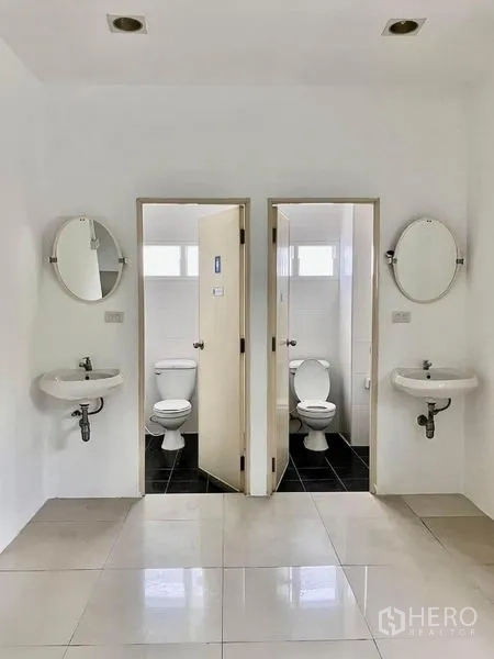 Warehouse for rent in Prawet, Bangkok - Twin restrooms with white tiles, basins, mirrors, and separate cubicles.