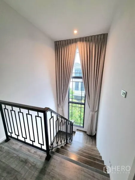Detached House for rent - Staircase with black metal railing and a tall window with curtains.