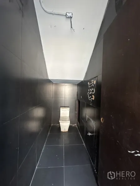 Home Office for rent in Pathum Wan, Bangkok - Narrow black-tiled restroom with a modern toilet and exposed ceiling conduit.
