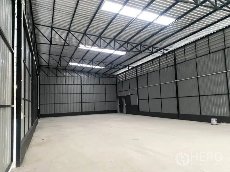 Warehouse for rent in Wang Thonglang, Bangkok - Bright warehouse interior highlighting high ceiling, skylight panels and rear access door.