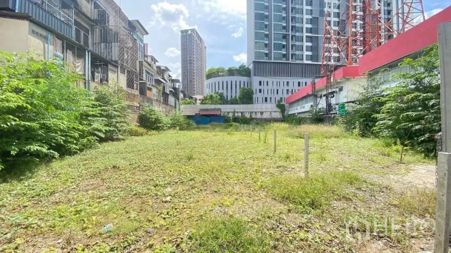 Land for rent in Watthana, Bangkok - Vacant land plot with grassy surface between low-rise shophouses and modern condos in Phra Khanong, Bangkok, under a sunny sky.