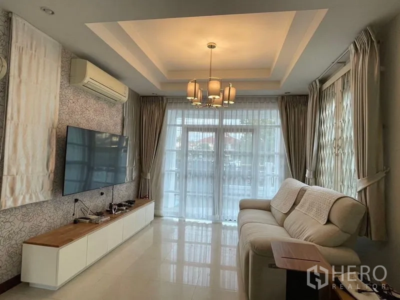 Detached House for rent in Bang Kapi, Bangkok - Living room with TV wall, sofa, cove ceiling lights and full-height curtains.