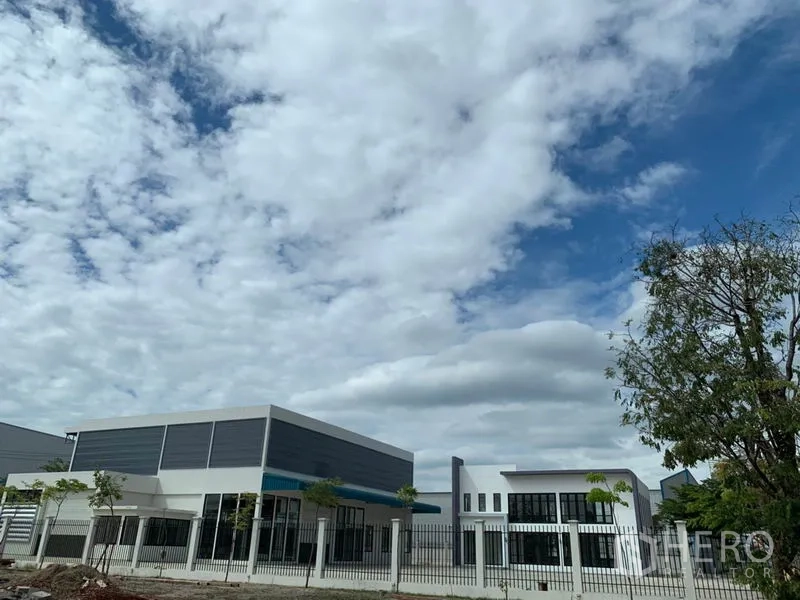 Warehouse for rent in Bang Phli, Samut Prakan - Modern warehouse and two-storey office within a fenced industrial compound under a cloudy blue sky in Bang Phli, Samut Prakan.