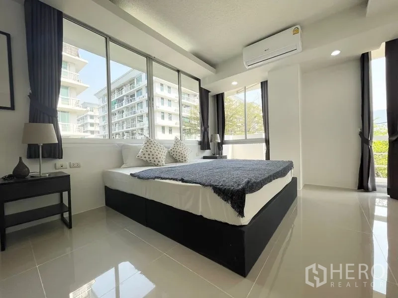 Condominium for rent in Khlong Toei, Bangkok - Bedroom with wide corner windows overlooking greenery and buildings.