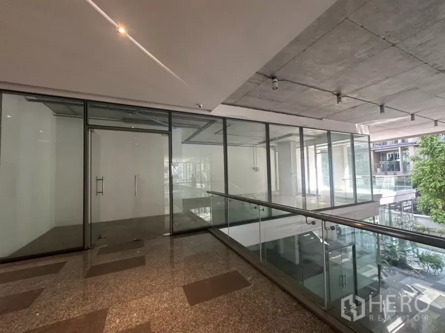 Retail Space for rent - Glass-front retail unit on an upper-level corridor with granite flooring and exposed concrete ceiling in Phra Khanong.
