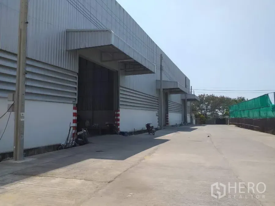 Warehouse for rent in Pak Kret, Nonthaburi - Modern warehouse exterior with covered loading bays and a wide concrete driveway in Pak Kret.