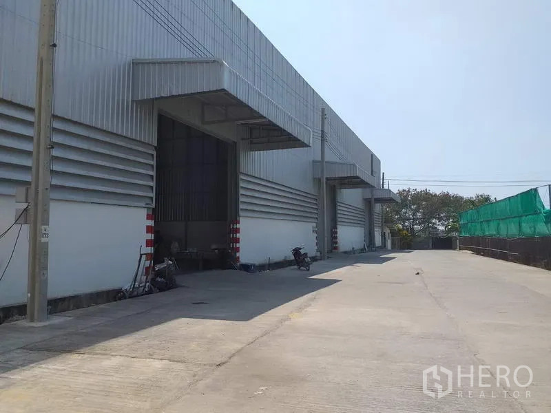 Warehouse for rent in Pak Kret, Nonthaburi - Modern warehouse exterior with covered loading bays and a wide concrete driveway in Pak Kret.