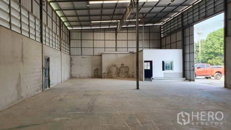 Warehouse for rent in Pathum Thani - Warehouse interior featuring a built-in office room and street-facing shutter entrance.