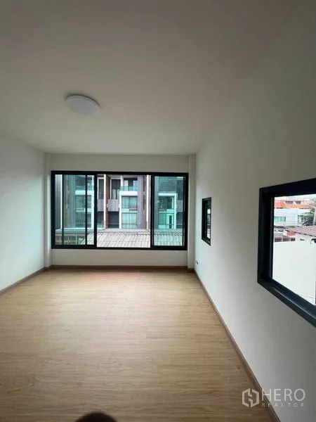 Home Office for sale - Empty office room with a long window wall and warm wood-look floors.