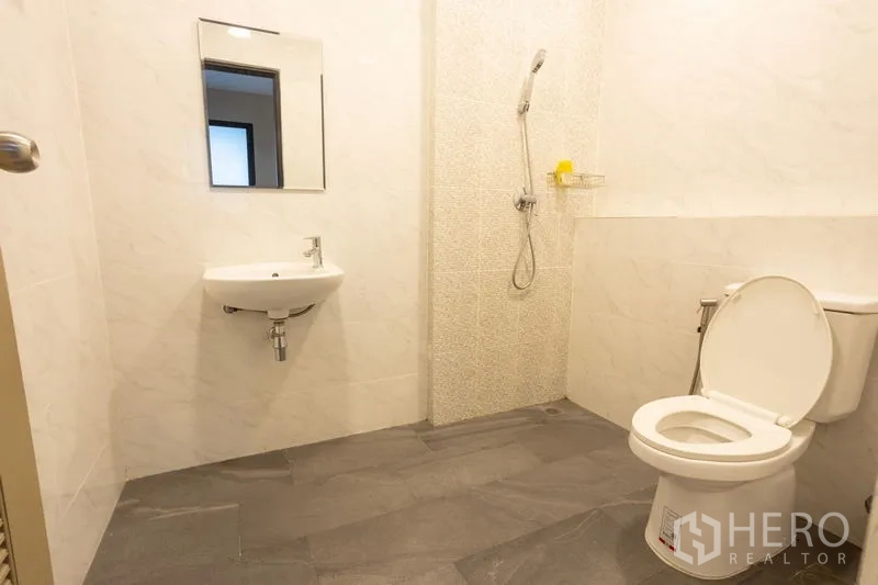 Home Office for rent in Bang Khen, Bangkok - Clean bathroom with wall-mounted sink, toilet and handheld shower on gray tile flooring.