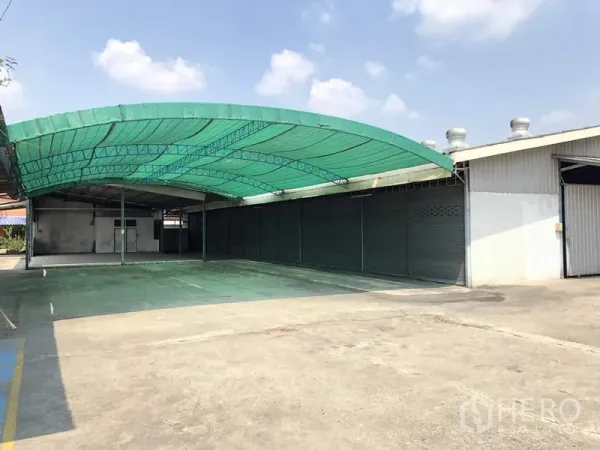 Warehouse for rent in Khlong Luang, Pathum Thani - Large covered loading bay with green canopy and multiple roller shutter bays beside the warehouse.