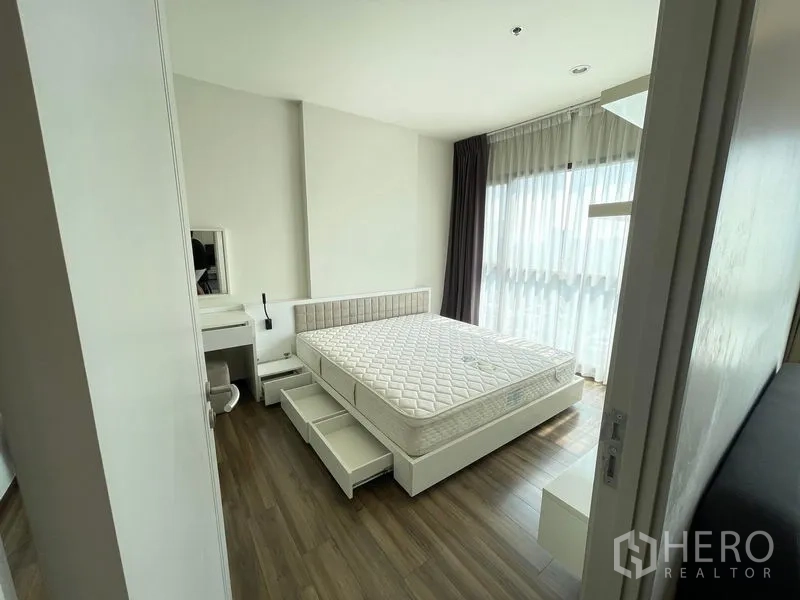 Condominium for rent in Khlong Toei, Bangkok - Sunlit master bedroom with storage bed, corner windows and sheer curtains.