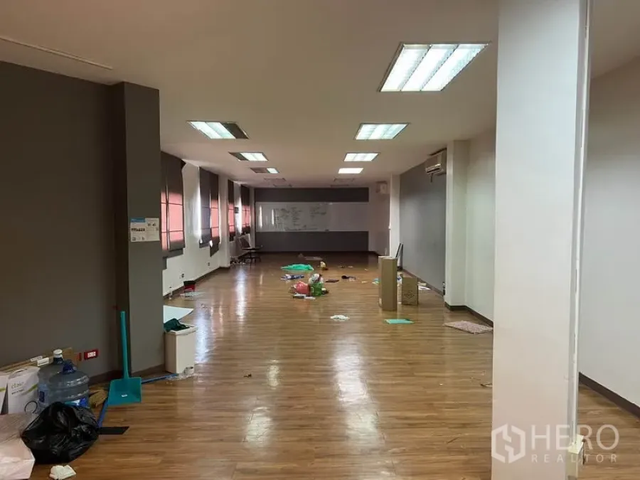 Office Space for rent in Khlong Toei, Bangkok - Open-plan office with wood floors, fluorescent ceiling lights, long windows with blinds and a whiteboard at the far end.