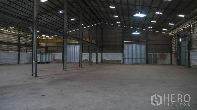 Factory for rent in Bang Phli, Samut Prakan - Spacious warehouse interior with high steel truss roof, concrete floor and large roller doors.