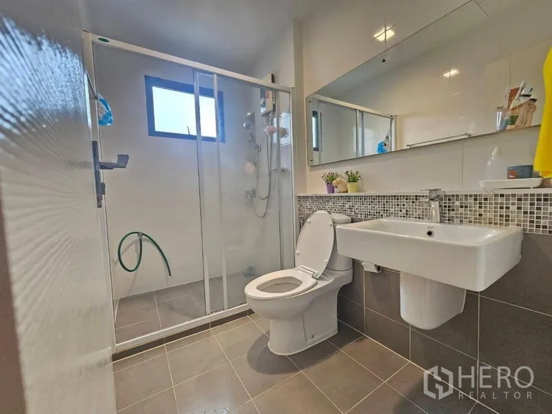 Detached House for sale in Prawet, Bangkok - Bathroom with glass‑enclosed shower, long mirror, toilet and wall‑mounted sink.