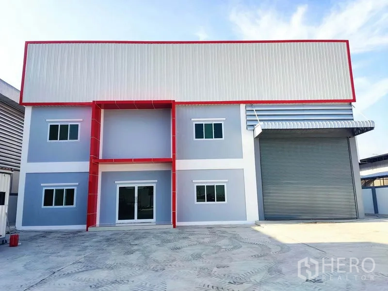 Factory for sale in Mueang Samut Sakhon, Samut Sakhon - Modern factory facade in grey with red trim, glass entrance and large roller shutter.