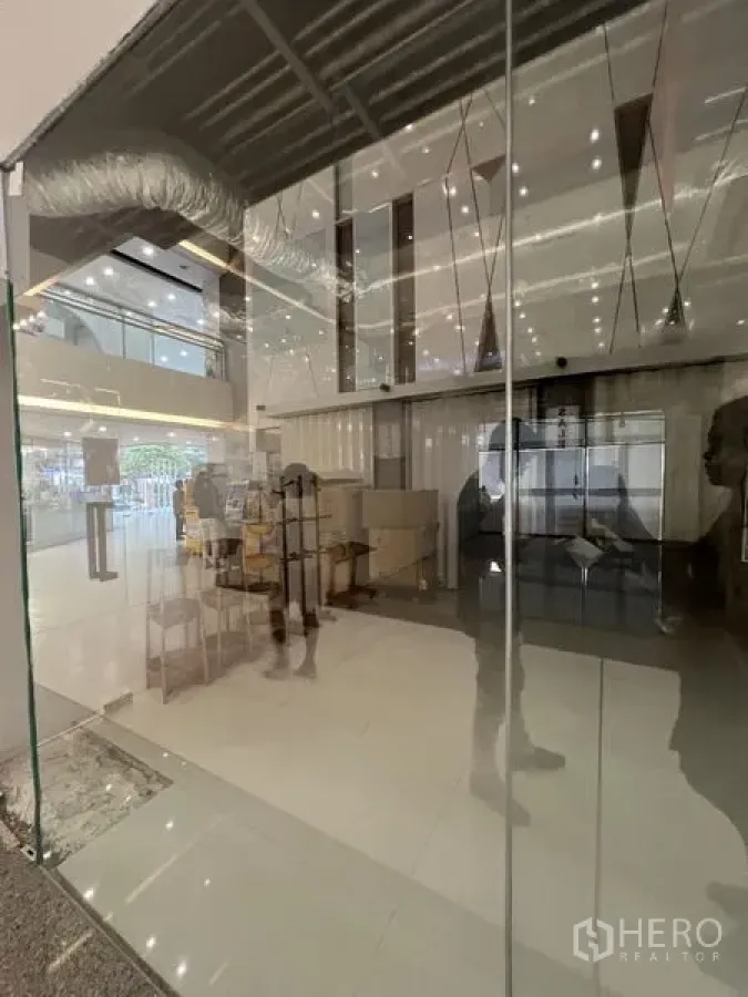 Retail Space for rent - Close-up of floor-to-ceiling glass facade showing interior lighting and atrium surroundings.