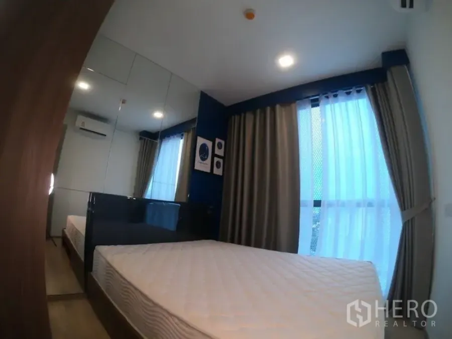 Condominium for rent or sale in Watthana, Bangkok - Cozy bedroom with mirrored wardrobe, blue accent wall and floor-to-ceiling curtains.