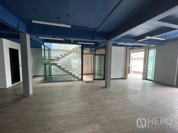 Office Space for rent in Watthana, Bangkok - Open-plan office with blue ceiling, wood-look floors and a glass-walled staircase core.