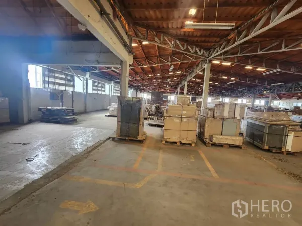 Factory for rent in Mueang Samut Sakhon, Samut Sakhon - Spacious warehouse interior with steel truss roof and pallets of boxed goods.