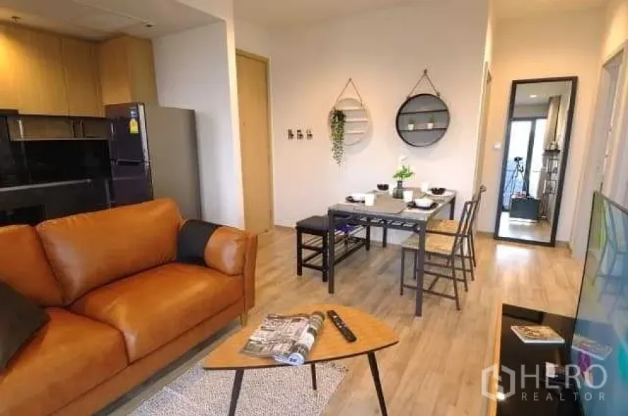 Condominium for rent or sale in Chatuchak, Bangkok - Open-plan living and dining area with leather sofa, compact kitchen and wood flooring.