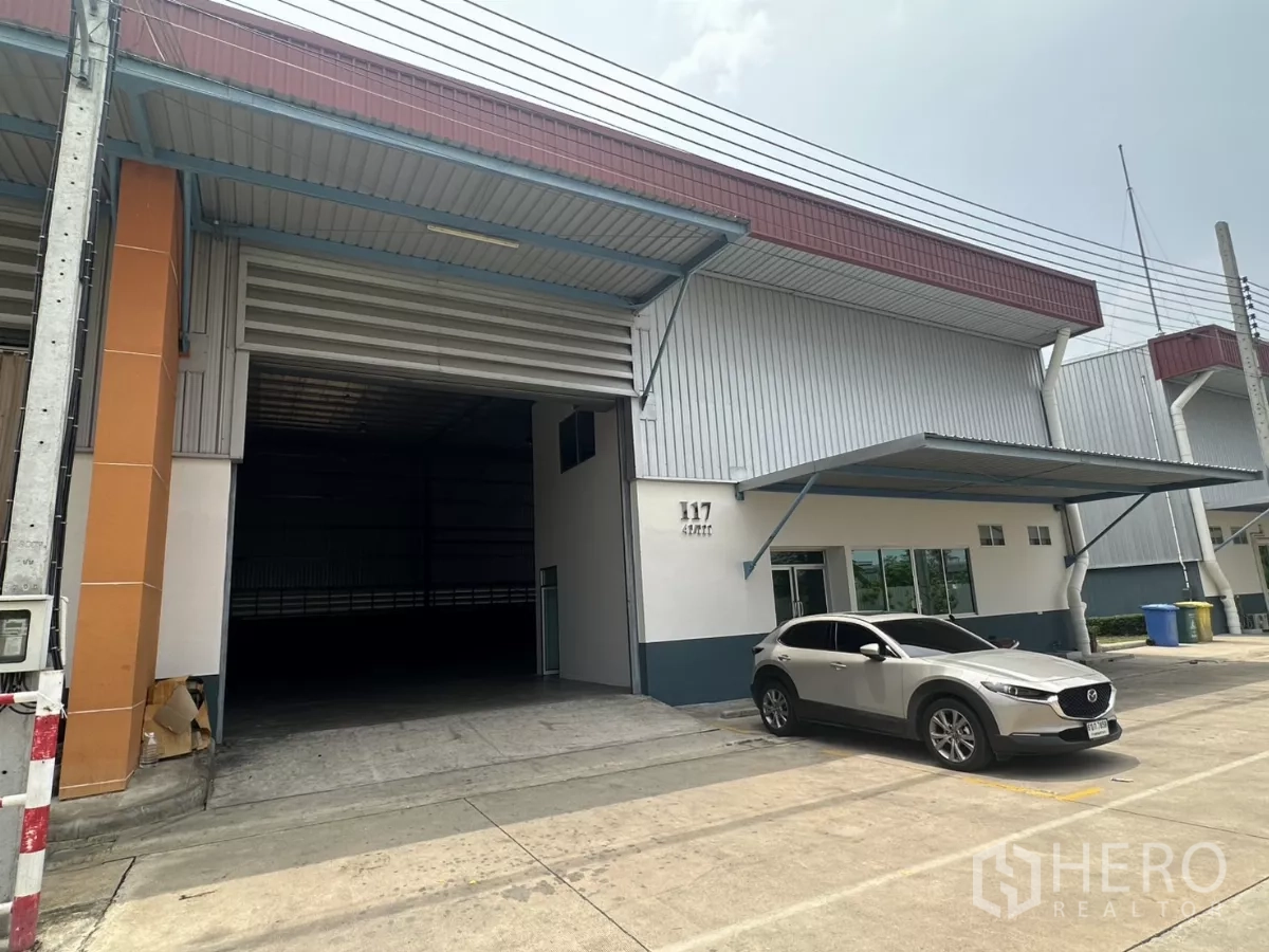 Factory for rent in Bang Phli, Samut Prakan - Factory facade with awning, parking space and partially open roller shutter.