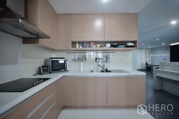 Condominium for rent in Khlong Toei, Bangkok - Modern L-shaped kitchen with built-in cabinets, electric cooktop, hood, microwave and sink.