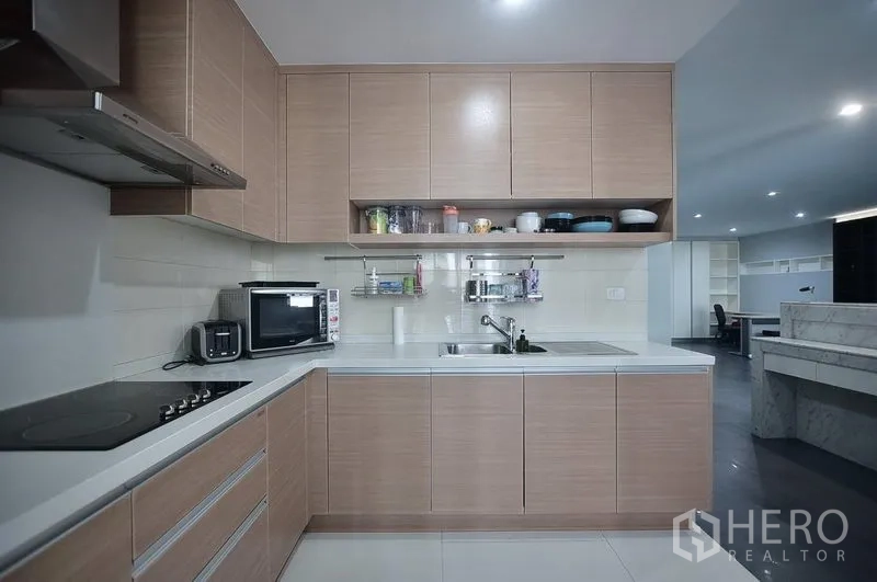 Condominium for rent in Khlong Toei, Bangkok - Modern L-shaped kitchen with built-in cabinets, electric cooktop, hood, microwave and sink.