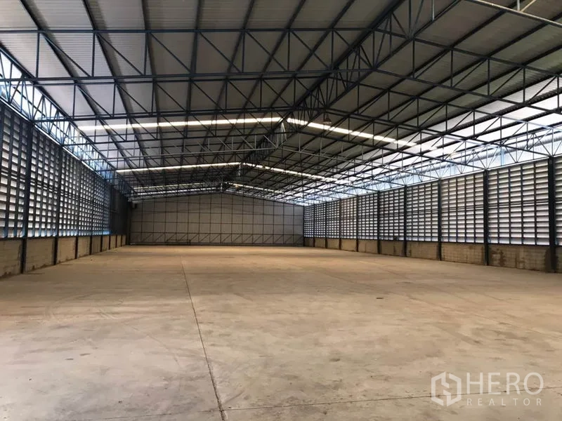 货栈 出租在Khlong Sam Wa, Bangkok - 宽敞仓库内景，高钢桁架屋顶、百叶通风墙与平整混凝土地面，屋顶透光板采光充足。