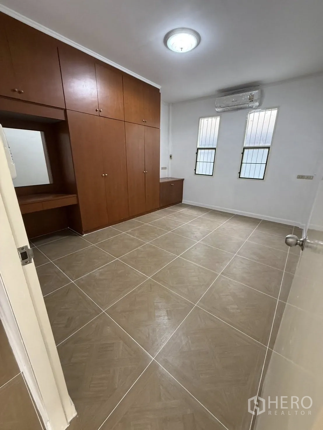 Detached House for rent in Khlong Toei, Bangkok - Bedroom with built-in wooden wardrobes, tiled floor, air conditioner, and tall windows.