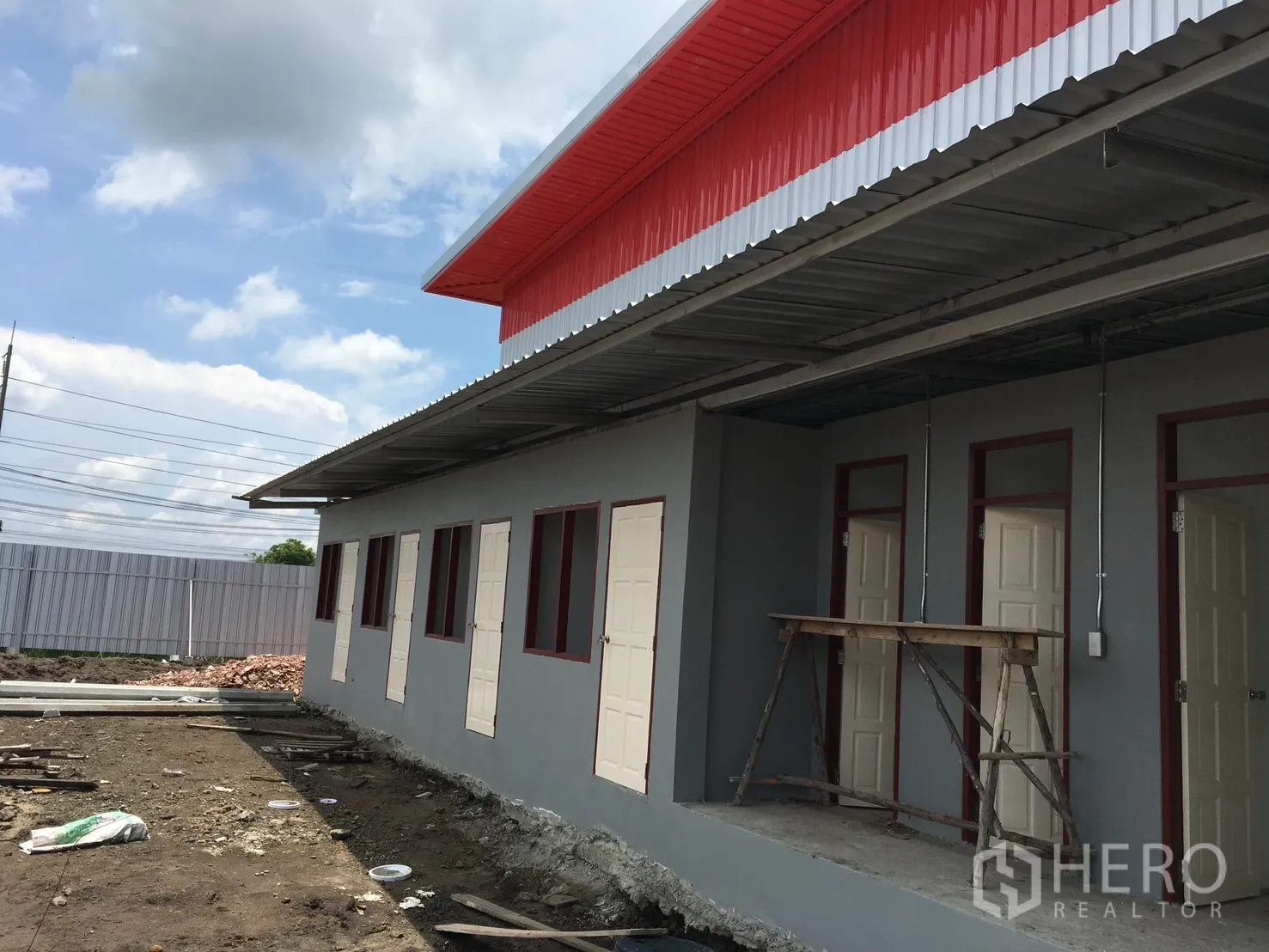 Warehouse for sale in Sai Noi, Nonthaburi - Side of the building with multiple doors under a covered walkway and visible utility work in progress.