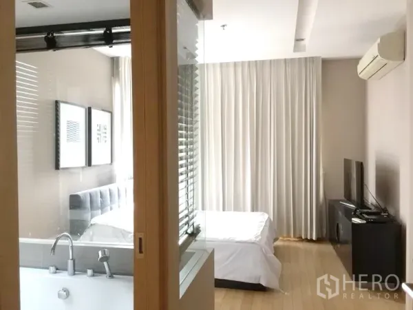 Condominium for rent in Khlong Toei, Bangkok - Master bedroom with glass-partition bathroom and bathtub, bed, TV console and wall-mounted air conditioner.