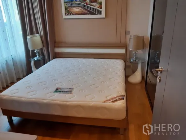 Condominium for rent in Khlong Toei, Bangkok - Bright bedroom with queen bed, bedside lamps, framed artwork, wardrobe and a large window.