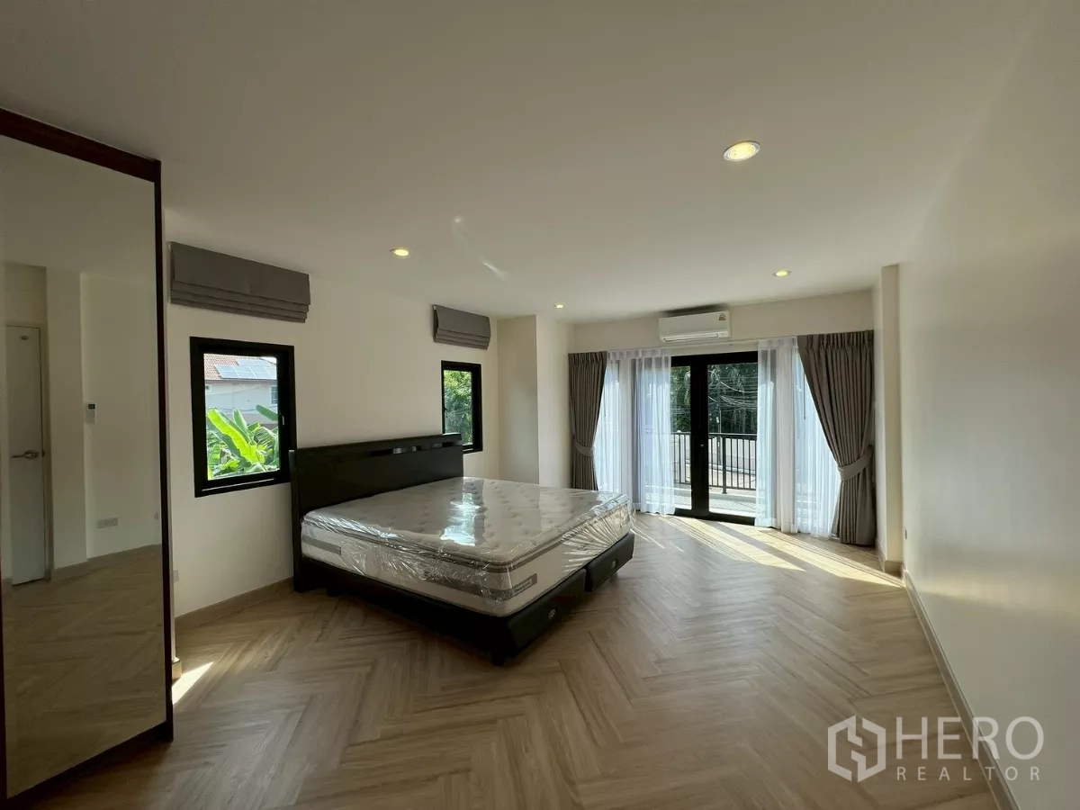 Detached House for rent in Suan Luang, Bangkok - Spacious master bedroom with balcony access, king bed, and herringbone wood flooring.