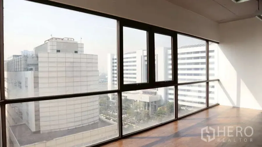 Office Space for rent - Corner office with floor-to-ceiling windows, wood flooring and panoramic city views of modern buildings.