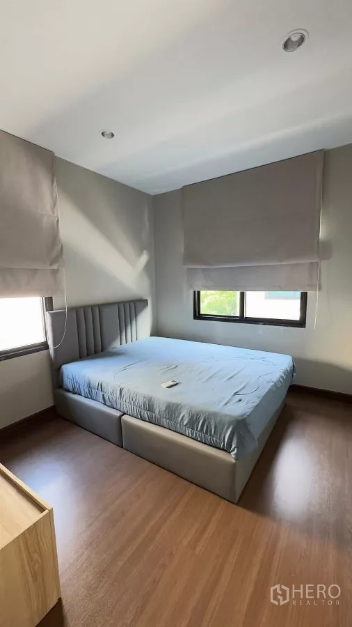 Detached House for rent in Samut Prakan - Guest bedroom with two windows, blinds and an upholstered bed.