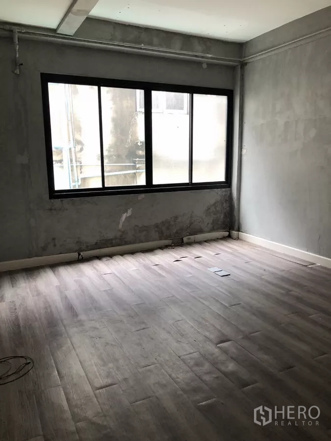 Shophouse for sale in Watthana, Bangkok - Large room with big window, concrete walls and laminate flooring.