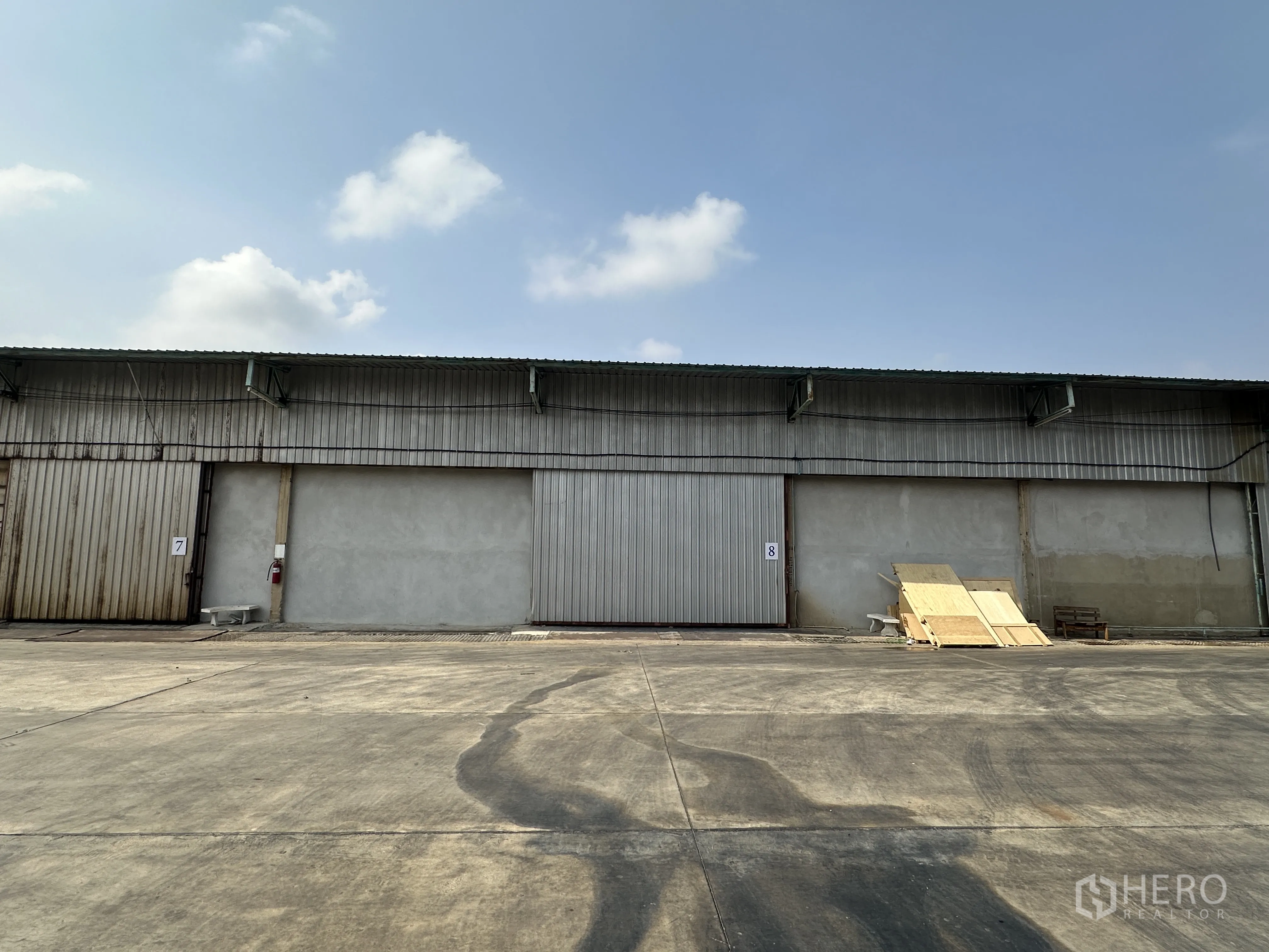 货栈 for rent in Mueang Pathum Thani, Pathum Thani - 金属外墙仓库外立面，超大滑动门与宽阔混凝土堆场，天空晴朗。