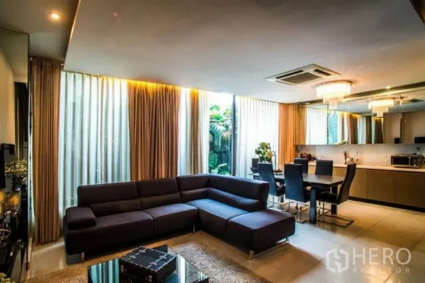 Townhouse for rent or sale in Watthana, Bangkok - Bright lounge and dining area with corner sofa, dining set and tall curtains