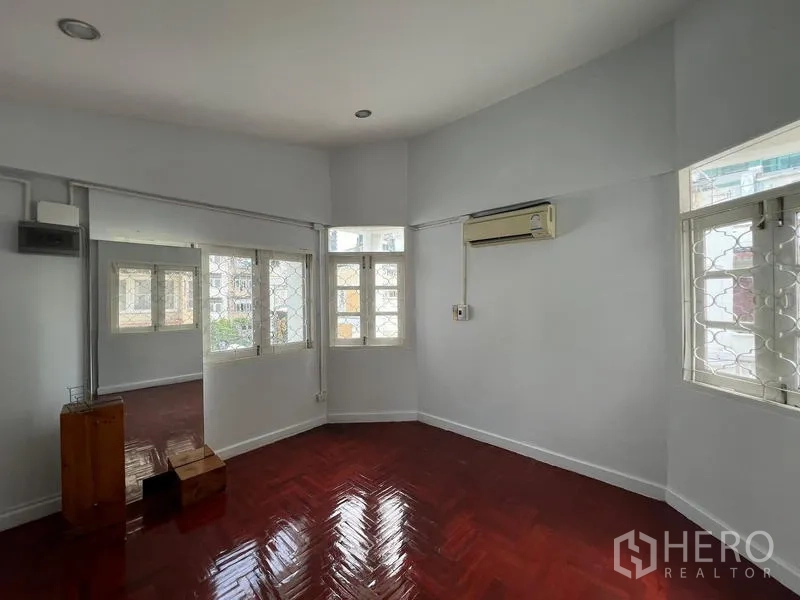 Home Office for rent in Watthana, Bangkok - Corner bedroom with air conditioner, multiple windows, and polished wooden floor.