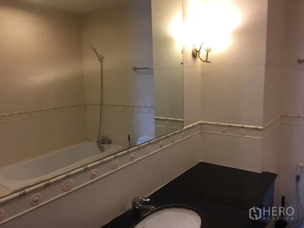 Condominium for rent in Khlong Toei, Bangkok - Bathroom featuring a bathtub, handheld shower and wide mirror over a black countertop.