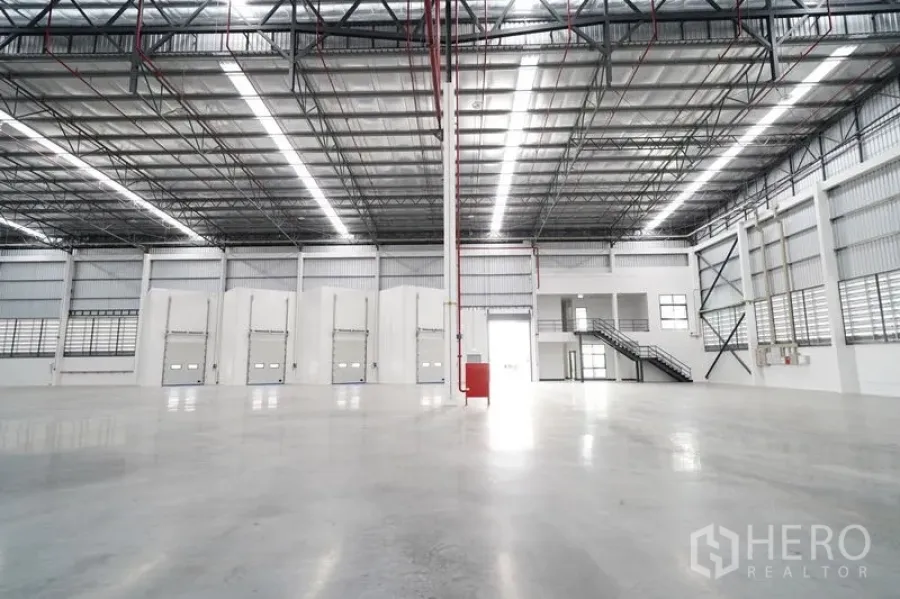 Warehouse for rent in Khlong Luang, Pathum Thani - Row of loading dock doors facing a spacious floor area and a two-story office with staircase.
