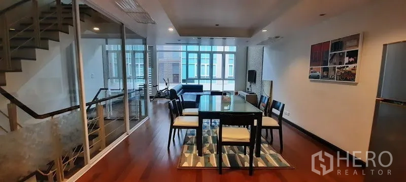 Townhouse for rent or sale in Khlong Toei, Bangkok - Dining zone beside a glass-partition staircase with hardwood flooring and ample natural light.